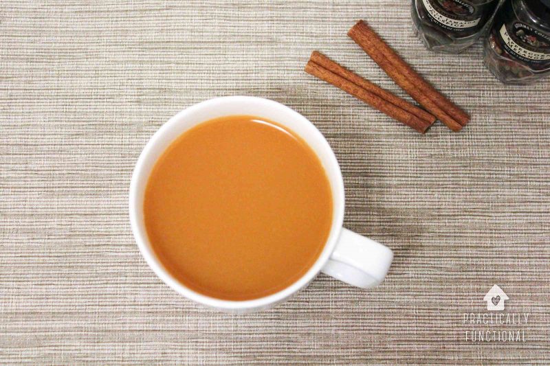 cup of homemade wassail cider in white mug with cinnamon sticks and spices