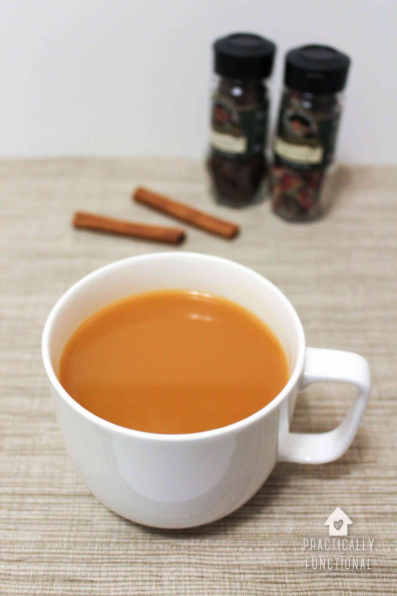 cup of homemade wassail cider in white mug with cinnamon sticks and spices in background